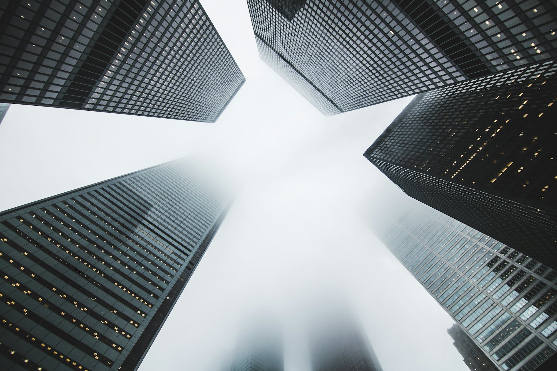 Glass towers seen from street level, converging against a pale sky